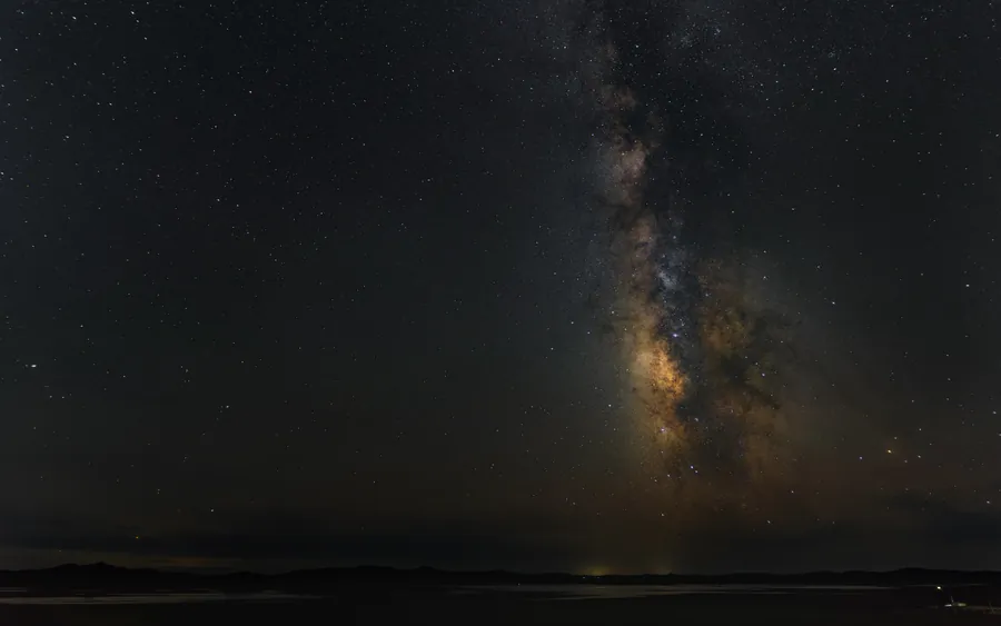 明亮银河纵贯夜空,金色星云延伸至暗色地平线,近处大地几乎隐入夜色。