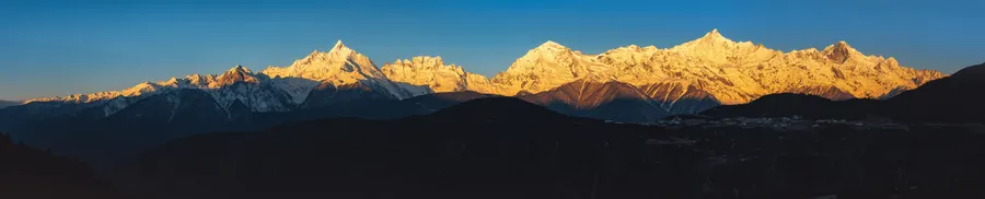 金色晨光照亮连绵雪峰,暗色山脊在前景层层展开。
