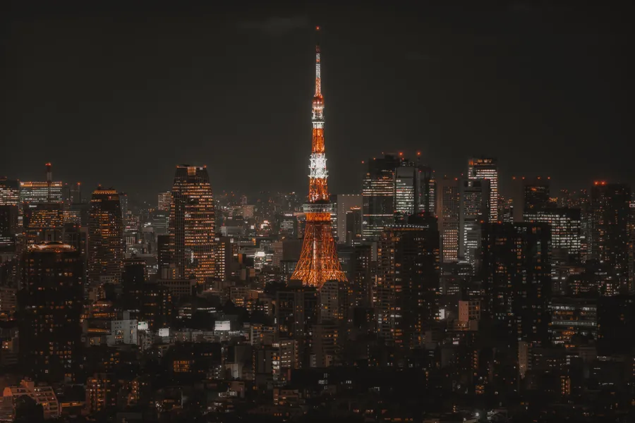 橙白色高塔在夜色中的密集楼宇之间亮起,城市灯火沿地平线延伸。