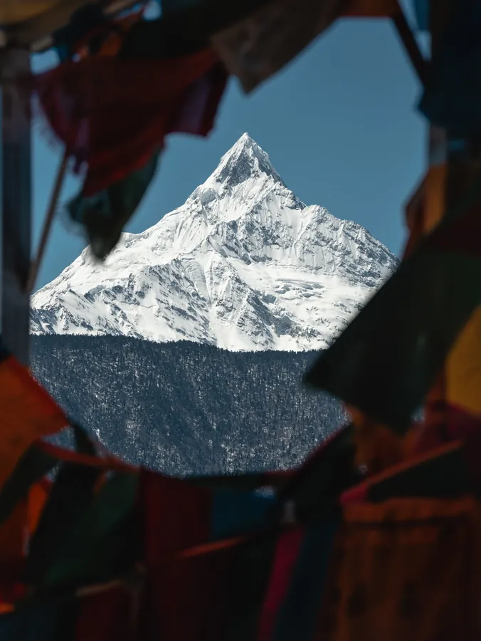 近处红色与深色布幡形成框景,中央露出明亮雪峰和暗色林线。